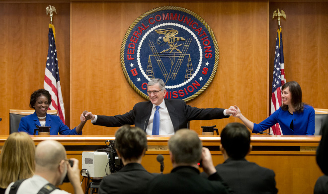 Federal Communication Commission (FCC) Chairman Tom Wheeler, center, joins hands with FCC Commissioners Mignon Clyburn, left, and Jessica Rosenworcel, before the start of their open hearing in Washington, DC, on Thursday, Feb. 26, 2015. 